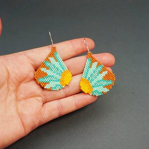 May include: A pair of beaded earrings with a teardrop shape. The earrings are made with turquoise, orange, and brown beads and feature a flower design.