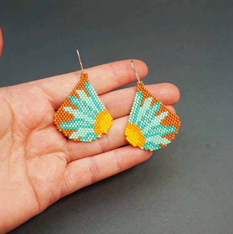 May include: A pair of beaded earrings with a teardrop shape. The earrings are made with turquoise, orange, and brown beads and feature a flower design.