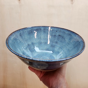 May include: A large, blue ceramic bowl with a speckled glaze. The bowl is slightly wider at the top than the bottom and has a rounded shape.