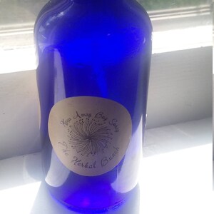 Puede incluir: Una botella de vidrio azul con un pulverizador negro y una etiqueta blanca que dice "Keep Away Bug Spray The Herbal Bunch".