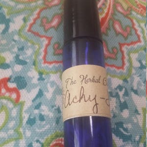 Puede incluir: Un frasco de vidrio azul con un rodillo y una etiqueta marrón que dice "The Herbal Blend Achy-Do".