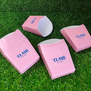 May include: A collection of light pink paper food containers with an open top and a tapered base. Each container features the blue text TLMB EST 2018 printed on the front. The set includes several stacked units and individual pieces.