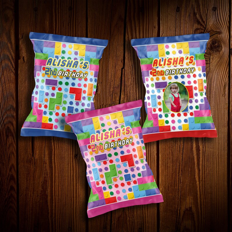 May include: Three colorful chip bags with a Lego-themed design. The bags are decorated with colorful blocks, dots, and a photo of a child. The text on the bags reads "Alisha's 2nd Birthday".