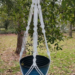 May include: White macrame plant hanger with a blue planter hanging from a tree branch.
