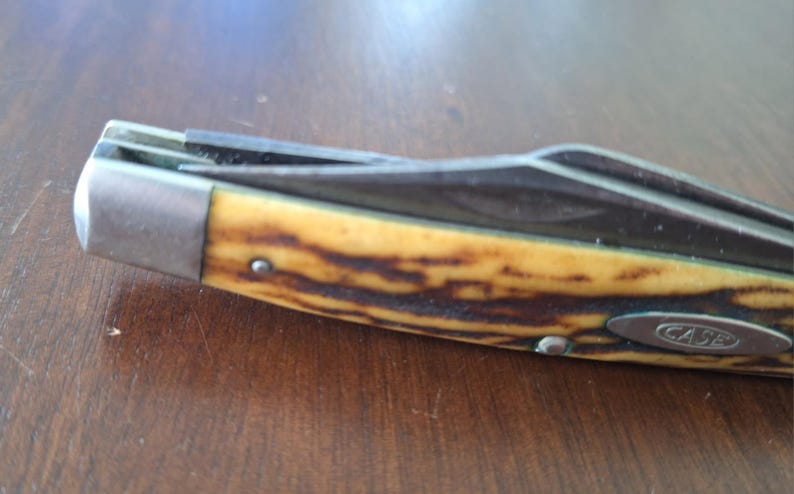 Puede incluir: Primer plano de una navaja de bolsillo con mango amarillo y marr&oacute;n y hoja plateada. La navaja tiene una virola met&aacute;lica y la palabra "CASE" es visible en el mango.