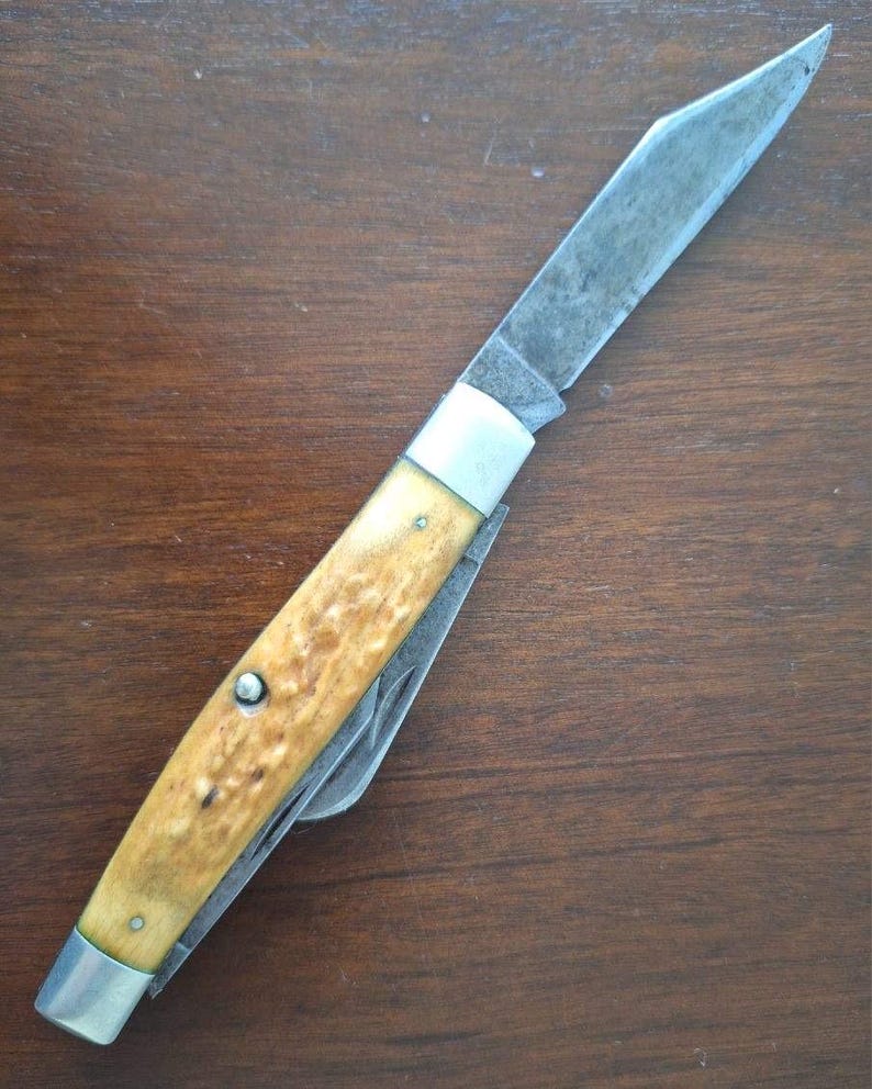 Puede incluir: Una navaja de bolsillo vintage con una hoja de acero inoxidable desgastada y un mango con un patr&oacute;n texturizado marr&oacute;n claro. La navaja tiene virolas plateadas y remaches. La hoja est&aacute; parcialmente abierta, revelando una hoja secundaria m&aacute;s peque&ntilde;a.
