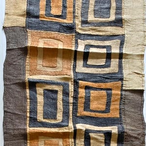 Peut inclure: Un chemin de table rectangulaire en textile présentant un motif géométrique répétitif de carrés et de rectangles imbriqués dans des tons brun foncé, beige et jaune doré. Le tissu a une texture tissée visible avec des coutures.