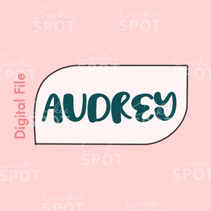 Może przedstawiać: Biała foremka do ciasteczek z czarnym obramowaniem w kształcie dymku. Wewnątrz dymku napis "AUDREY" w ciemnoniebieskim kolorze.