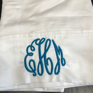 May include: White pillowcase with a blue embroidered monogram of the letters "EFM".