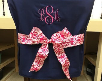 May include: A navy blue chair cover with a pink monogram "BSH" and a white and pink damask ribbon tied in a bow.