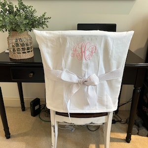 May include: White chair cover with a white satin bow and pink embroidered monogram "HHP".