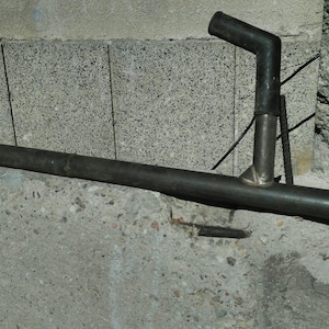 Peut inclure: Un tuyau en métal noir avec une extrémité incurvée et un capuchon rond. Le tuyau est fixé à un mur en béton.