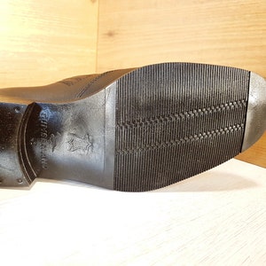 May include: Close-up of the black leather sole of a shoe with a textured pattern. The sole is marked with the words "Genuine Leather" and "Made in Thailand".
