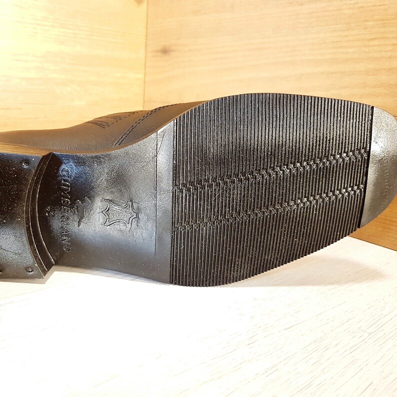 May include: Close-up of the black leather sole of a shoe with a textured pattern. The sole is marked with the words "Genuine Leather" and "Made in Thailand".