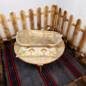 K&ouml;nnte beinhalten: Eine Holzsch&uuml;ssel steht auf einem runden Holztisch mit einer gemusterten Tischdecke. Der Tisch steht auf einem grauen und rot gestreiften Teppich. Ein Holzzaun umgibt den Tisch.