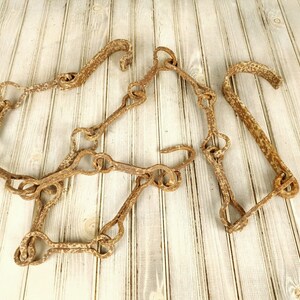 Może przedstawiać: Łańcuch z rdzewiejących metalowych haków, połączonych ze sobą, o rustykalnym, postarzanym wyglądzie. Łańcuch leży na jasnym drewnianym podłożu.