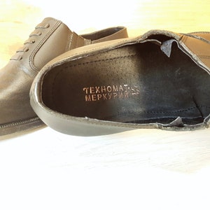 May include: A pair of black leather shoes with a brown inscription that reads "TEHNOMAT-ES MERKURIJ-ES".