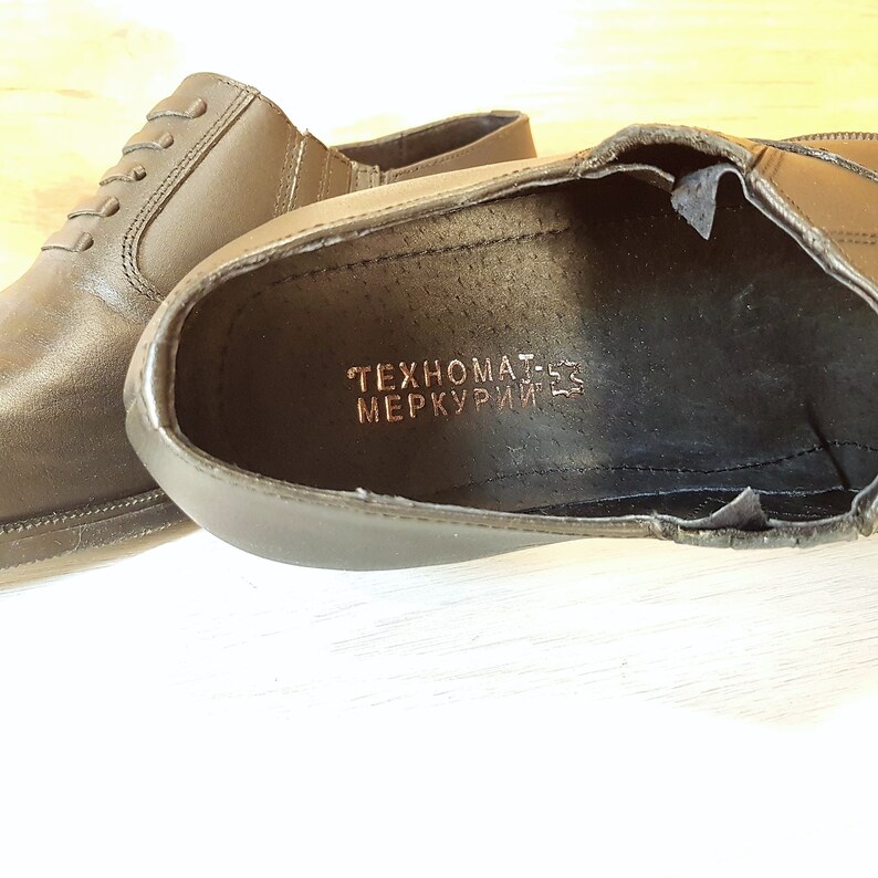May include: A pair of black leather shoes with a brown inscription that reads "TEHNOMAT-ES MERKURIJ-ES".