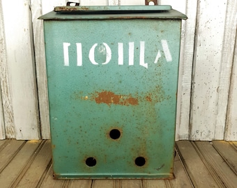 Può includere: Una scatola di metallo verde con la parola "TOILLA" scritta in vernice bianca. La scatola ha un coperchio incernierato e diversi fori nella parte anteriore.
