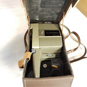 May include: A vintage brown leather camera case with a silver and black Avrora 8mm film camera inside. The camera has a silver lens and a black handle.