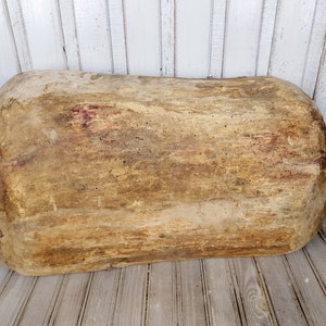 K&ouml;nnte beinhalten: Eine gro&szlig;e, ovale Holz-Teigsch&uuml;ssel mit nat&uuml;rlicher, rustikaler Oberfl&auml;che. Die Sch&uuml;ssel ist hellbraun mit dunkleren braunen Streifen und Flecken.