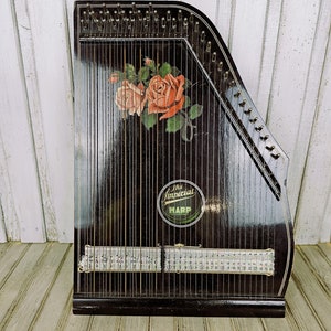 Può includere: Una cetra vintage nera The Imperial Harp con un design floreale e una chiave di accordatura dorata. La cetra ha un corpo in legno nero e una tavola armonica in metallo.