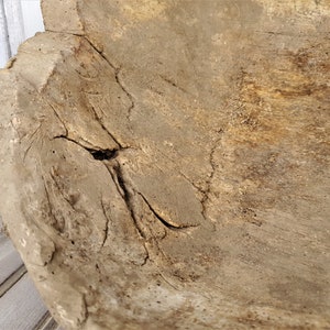 K&ouml;nnte beinhalten: Eine gro&szlig;e Holzsch&uuml;ssel mit nat&uuml;rlicher, rustikaler Oberfl&auml;che. Die Sch&uuml;ssel hat eine tiefe, abgerundete Form und zeigt Spuren von Alter und Gebrauch, einschlie&szlig;lich Risse und Unvollkommenheiten. Das Holz ist hellbraun mit dunkleren braunen Streifen.