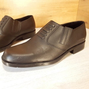 May include: A pair of black leather slip-on shoes with a decorative stitching detail on the top.