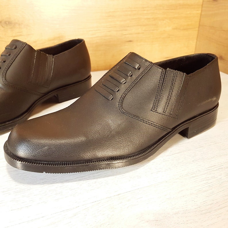 May include: A pair of black leather slip-on shoes with a decorative stitching detail on the top.