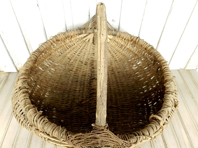 K&ouml;nnte beinhalten: Ein gro&szlig;er, runder Korb aus geflochtenem Material mit einem langen, h&ouml;lzernen Griff. Der Korb ist aus nat&uuml;rlichen Materialien gefertigt und hat einen rustikalen, Vintage-Look.