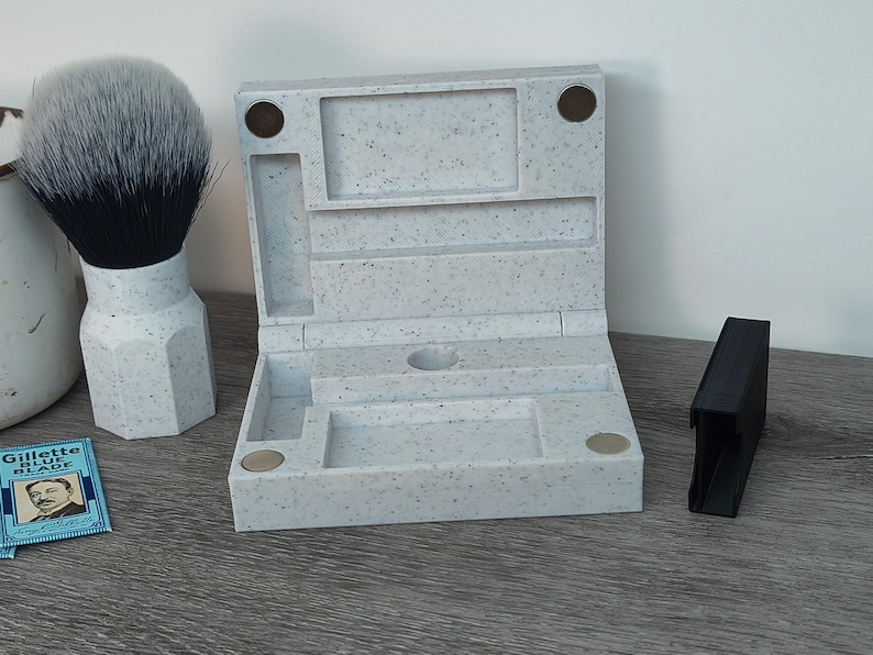 May include: A light gray speckled shaving kit with a hinged lid, compartments, and a black handle. A shaving brush with a white handle and black bristles is to the left. A blue and white Gillette Blue Blade package is visible.