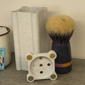 May include: A shaving set comprising a shaving brush with a dark blue handle and a light-coloured bristle head, a speckled white soap dish, and a speckled white razor holder. Two vintage Gillette Blue Blade packs are also visible.
