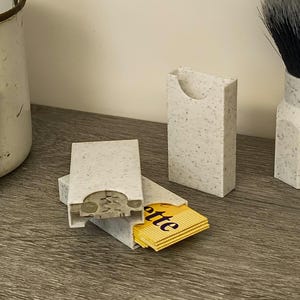 May include: A set of speckled gray razor blade holders, one open with yellow Gillette blades visible. A shaving brush and vintage Gillette Blue Blade box are also present, suggesting a grooming theme.