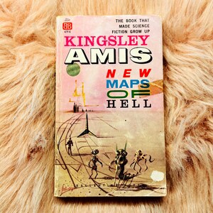 May include: Vintage paperback book titled "New Maps of Hell" by Kingsley Amis. The cover features a pink and white background with illustrations of rockets and alien figures. The book is set against a backdrop of fluffy, light brown fur.