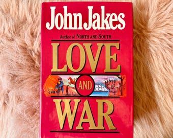 May include: A red hardback book titled "Love and War" by John Jakes, author of "North and South". The cover features a gold-coloured title and illustrations of people and ships.
