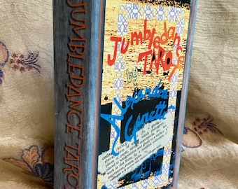 May include: A tarot card box with a distressed wood-grain design. The box features the title "Jumbleban by TAROT" in orange and blue lettering. The side of the box reads "JUMBLEDANCE TAROT" in orange. The box has a collage design.