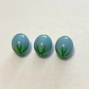 May include: Three light blue glass beads with green and white starburst designs.