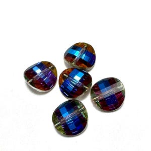 May include: Five iridescent, faceted beads with a mix of blue, purple, and gold tones. The beads have an irregular, organic shape and are scattered against a white background. These beads are suitable for jewelry making.