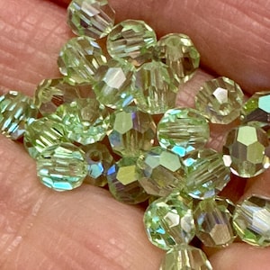 May include: A close-up of a pile of light green faceted glass beads. The beads are round and have a slight iridescent sheen.