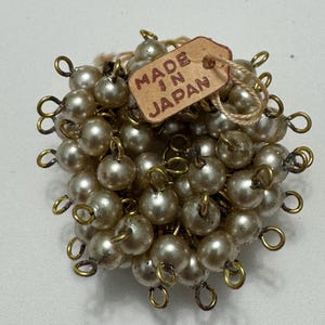 May include: Vintage pearl cluster brooch with gold-tone metal accents. The brooch is composed of numerous faux pearls, each individually attached with a loop. A small tag reads "MADE IN JAPAN".