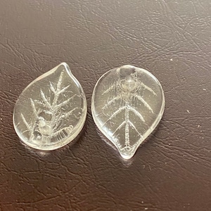 May include: Two clear glass leaf-shaped charms with a raised etched design of a branch with leaves.