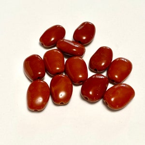 May include: A group of 12 brown oval-shaped beads. The beads are smooth and glossy.