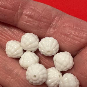 May include: A close-up of white, round, textured beads. The beads have a raised, flower-like design.