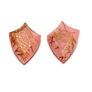 May include: A pair of pink resin earrings with gold leaf accents. The earrings are shaped like a pointed diamond.