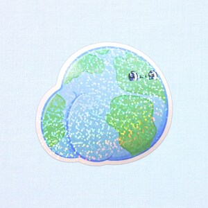 May include: A holographic sticker featuring a cartoon Earth with a smiling face. The continents are green, and the oceans are blue with sparkling accents. The sticker has a white border and is set against a light blue background.