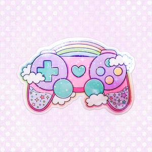 May include: A pastel-colored sticker of a video game controller with a rainbow, clouds, and stars. The controller features a cross-shaped directional pad, buttons, and a heart. The color scheme includes pink, purple, and teal.