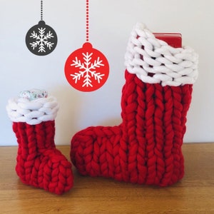 May include: Two red knitted Christmas stockings with white cuffs. The larger stocking is filled with a red gift box. The smaller stocking is filled with a wrapped gift.