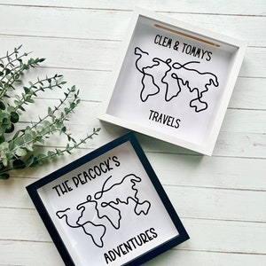 May include: Two square shadow boxes with a world map design. One box has a white frame with the text "Clem & Tommy's Travels". The other box has a black frame with the text "The Peacock's Adventures". Both boxes have a white background.