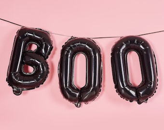 May include: Black foil balloons spelling out the word "BOO" are strung across a pink background. The balloons are inflated and have a shiny, reflective surface, perfect for Halloween decorations.