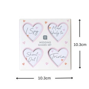 May include: A white square box with four pink heart-shaped frames. Each frame contains a wedding game idea: "I Spy", "Most Likely To", "Shout Out", and "Trivia". The box measures 10.3 inches by 10.3 inches.